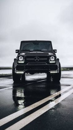 a black mercedes benz is driving down the road in the rain with its headlights on