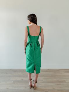 a woman in a green dress standing on a wooden floor with her back to the camera