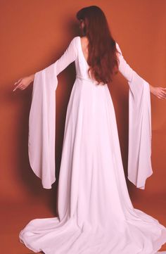 This is a stunning and rare 1960's fairytale renaissance vintage wedding dress - i have truly never seen one quite like this. it is a sleek white dress with two layers: a solid white underlay and a sheer white overlay. this zips closed in the back fitting the detailed beaded waist to your shape. the top of the dress is adorned with circle clusters of beads resembling a star or snowflake making this so lovely for a winter wedding. the true star is clearly the sleeves - they are long dramatic sheer draping sleeves that have very subtle flower clusters of sequins through out. this piece is in insane condition for age and does't show signs of wear. please note below for sizing and feel free to ask any questions you may have before purchasing.  brand bonny size 12 length front 60" length back 9 White Fitted Ethereal Dress, Ethereal White Fitted Gown, Ethereal Fitted Wedding Gown, White Long Sleeve Gown For Costume Party, Ethereal Fitted Floor-length Gown, Ethereal Fitted Dress For Wedding Night, Vintage White Dress For Costume Party, Medieval Style Fitted Formal Dress, White Fitted Gown For Costume Party