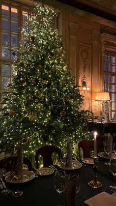 a large christmas tree is lit up in the middle of a dining room with tables and chairs