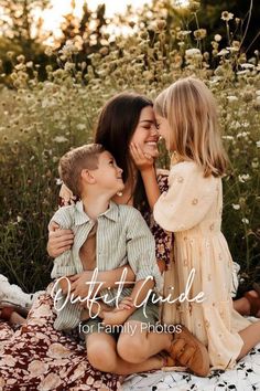 three children are sitting on a blanket in front of some wildflowers and one is kissing the other's cheek