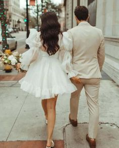 a man and woman are walking down the street holding hands, dressed in beige suits