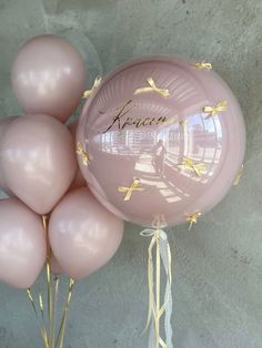 some pink balloons with gold foil lettering on them are sitting in front of a gray wall