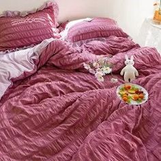 a bed covered in pink sheets and pillows with food on the bottom shelf next to it