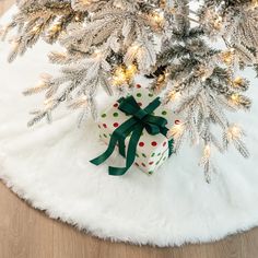 a present wrapped in green ribbon sitting under a christmas tree on a white fur rug