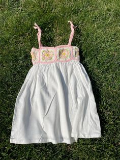 a white dress laying on the grass with pink trimmings and flowered details