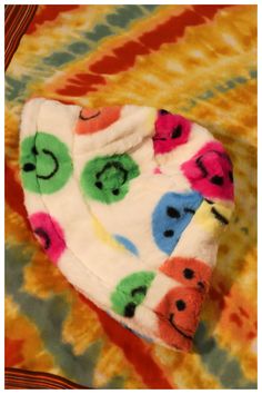 a multicolored tie dye hat with smiley faces on it sitting on a bed