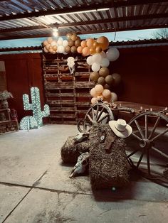 an old wagon with balloons attached to it in front of a wooden fence and cactus