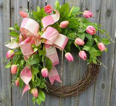 a wreath with pink tulips and green leaves hanging on a wooden fence outside