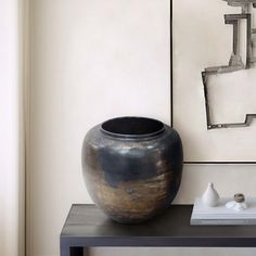 a black vase sitting on top of a table next to a white and gray wall