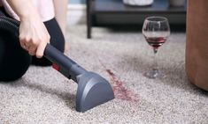 a woman is cleaning the floor with a vacuum and a glass of wine in front of her