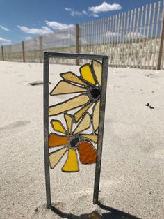 a stained glass window sitting on top of a sandy beach next to a metal fence