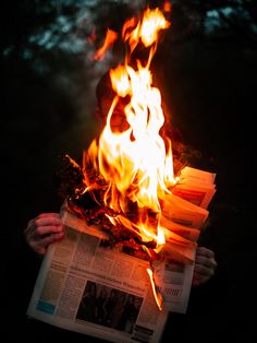 a person holding a newspaper in front of a fire with flames coming out of it