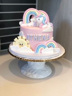 there is a pink cake with rainbows and clouds on the top that says athena