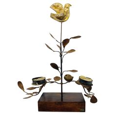 a metal sculpture with flowers and leaves on a wooden base, against a white background