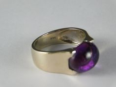 Jelly Bean Amethyst Cabochon Ring in !4K white gold. The ring features an oval amethyst that measures 12X10mm and by formula is 4.5 carats. The gemstone is set East to West and in a square top white gold mounting. The ring is solid 14K white gold and has a very good gold weight of 5.3 grams of solid gold. Currently a size 8, the ring can be sized up or down as needed. The ring is 10mm wide and tapers down to 4.85mm at bottom with a rise off of the finger of 7.29mm. Note that 6mm is approximately Formal Polished Amethyst Oval Cabochon Ring, Formal Oval Cabochon Amethyst Ring With Polished Finish, Collectible Oval Cabochon Amethyst Ring, Oval Cabochon Amethyst Ring For Formal Events, Oval Cabochon Amethyst Ring For Formal Occasions, Modern Amethyst Ring With Polished Finish, 14k Gold Polished Amethyst Ring, 14k Gold Amethyst Ring With Polished Finish, 14k Gold Round Amethyst Ring With Polished Finish