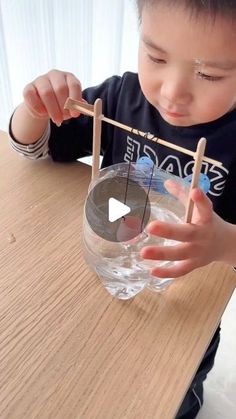 a young boy is playing with water in a bowl and clothes pins on the table