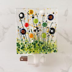 a glass block with buttons and flowers on it sitting on a wall next to a charger