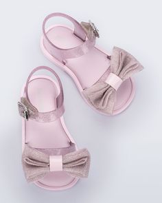 In this new style, the Mini Melissa Mar Sandal Sweet is donned with a petite layered bow appliqué, a glitter finish in varying colors, and an adjustable buckle closure for a safe and secure fit. Match with your little or pick a color for her to call her own. Pink Bow Sandals With Synthetic Material, Pink Synthetic Sandals With Bow, Pink Sandals With Bow Straps For Summer, Pink Open Toe Sandals With Bow Straps, Party Sandals With Bow Straps, Cute Pink Party Sandals, Pink Glitter Party Sandals, Adjustable Glitter Sandals For Party, Cute Bow Sandals With Round Toe