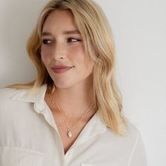 a woman with blonde hair wearing a white shirt and gold necklace, looking at the camera