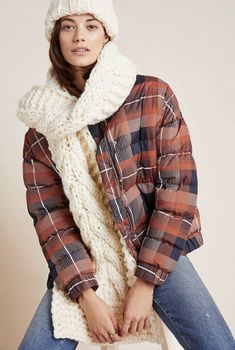 a woman in plaid jacket and hat sitting on top of a white box holding a handbag