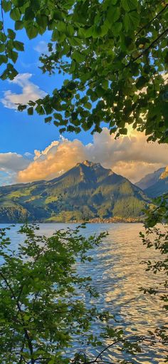 a lake surrounded by trees and mountains under a blue sky with clouds in the background