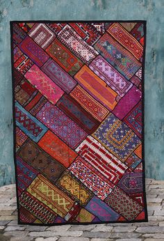 a multicolored patchwork quilt hanging on a wall in front of a brick floor