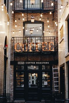 the outside of a coffee shop with lights strung from it's ceiling and windows