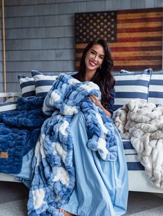 a woman is sitting on a bed covered in blue and white blankets with an american flag behind her