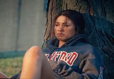 a woman sitting in front of a tree with her head on the ground and eyes closed