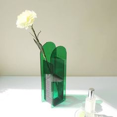 a flower in a green vase next to an empty bottle on a white counter top