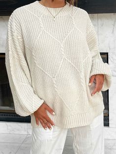 a woman standing in front of a fireplace wearing a white sweater and white pants with her hands on her hips