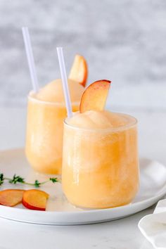 two glasses filled with orange juice and garnished with sliced peaches on a white plate