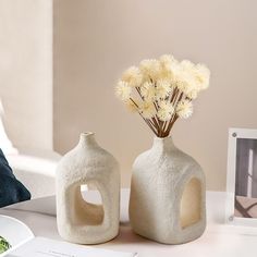 two white vases with flowers in them sitting on a table next to a photo frame