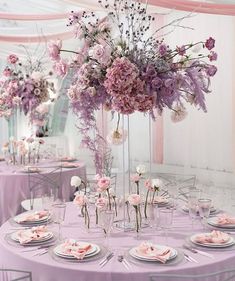 the table is set with pink and purple flowers in vases, plates and napkins