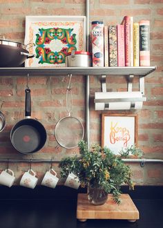 pots and pans are hanging on the wall next to a pot rack with books