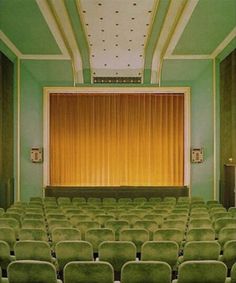 an empty auditorium with rows of green chairs and a yellow curtain on the stage behind it