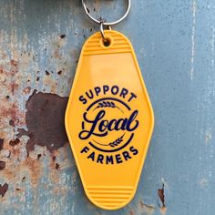 a yellow keychain hanging from the side of a rusted metal door that says support local farmers