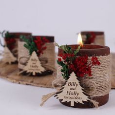 three small candles are decorated with burlocks and red flowers, one candle has a christmas tree on it