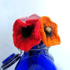 two crocheted flowers are placed in a blue glass vase with a white background