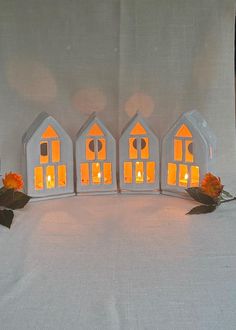 three small white houses are lit up with candles and roses on the table next to each other