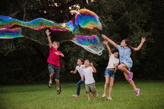 four children are playing with bubbles in the grass and one child is jumping up into the air