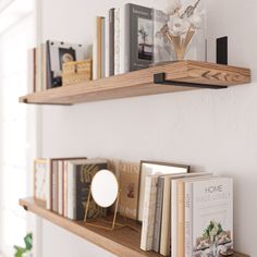 two wooden shelves with books on them in front of a white wall and potted plant