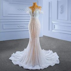 a wedding dress on display in a room with white walls and grey carpeted flooring