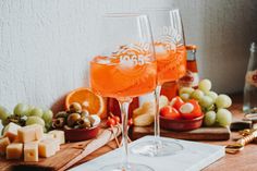 two glasses filled with wine sitting on top of a wooden table next to cheese and fruit