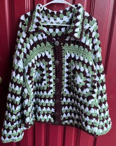 a crocheted sweater hanging on a red door with a green and white pattern