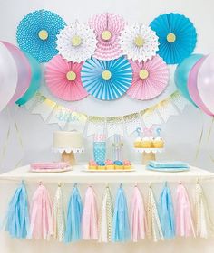 a table topped with cake and balloons next to a wall covered in paper fan decorations