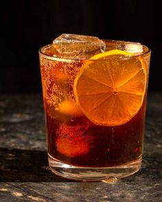 a close up of a drink with an orange slice on the rim and ice cubes