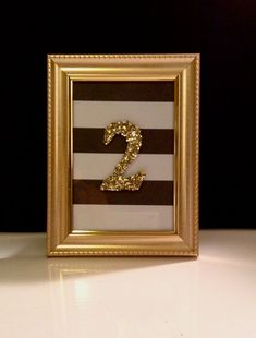 a gold and white frame with the number two in it's center is sitting on a table