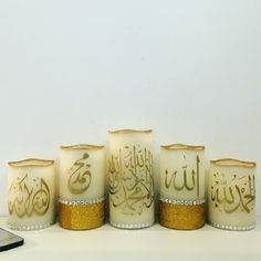 four candles with arabic writing on them next to a cell phone